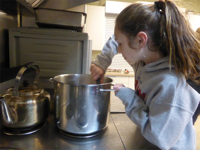 A child stirs a pot in a kitchen